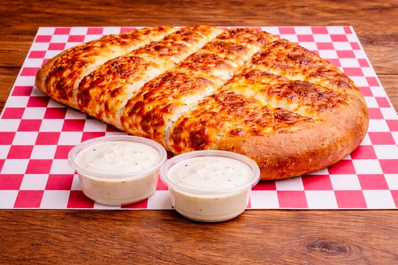 Cheesy breadsticks with two dipping sauces on red and white checkered paper.