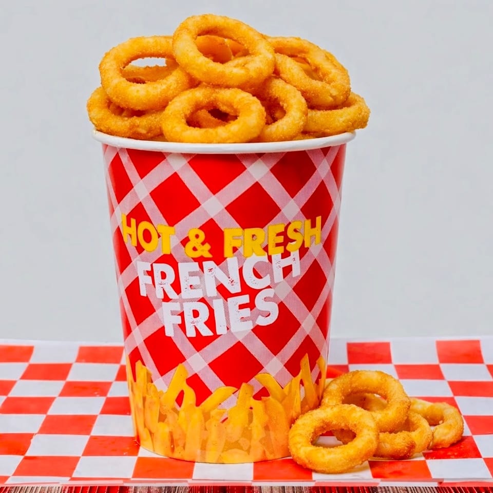Golden onion rings overflowing from a red and white checkered cup labeled "Hot & Fresh French Fries".