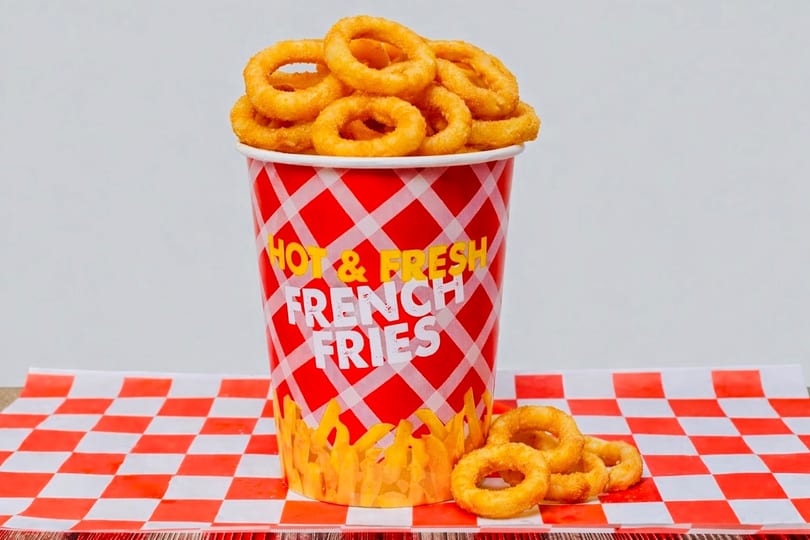 Golden onion rings overflowing from a red and white checkered cup labeled "Hot & Fresh French Fries".