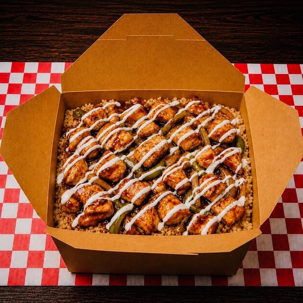Chicken and vegetables with sauce and drizzle in a brown takeout box on a red and white checkered paper.
