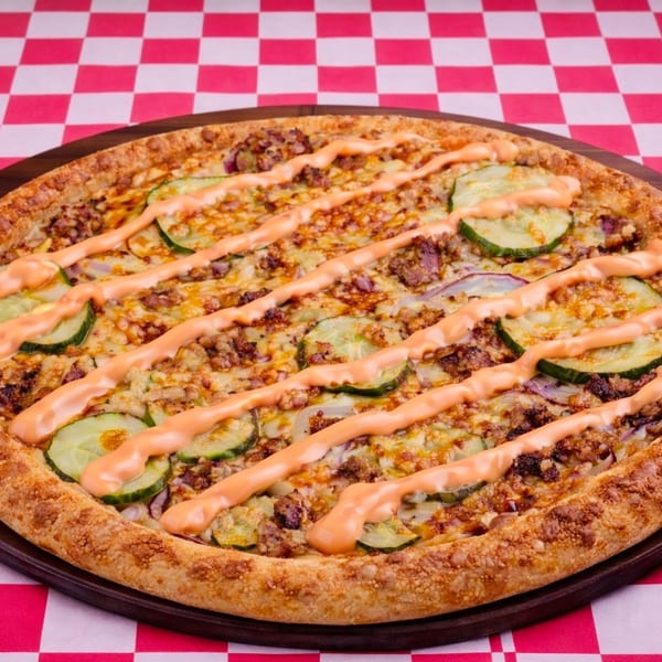 A pizza with ground meat, red onion, cucumber slices, and orange sauce on a red and white checkered tablecloth.