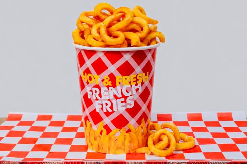 A red and white checkered cup overflowing with golden curly fries on a matching checkered paper.