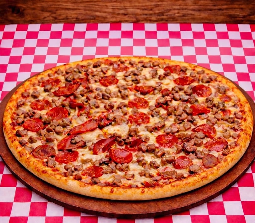 A large pepperoni and sausage pizza on a wooden board, resting on a red and white checkered tablecloth.