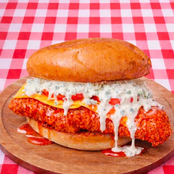 Spicy fried chicken sandwich with cheese, blue cheese dressing, and diced tomatoes on a bun.