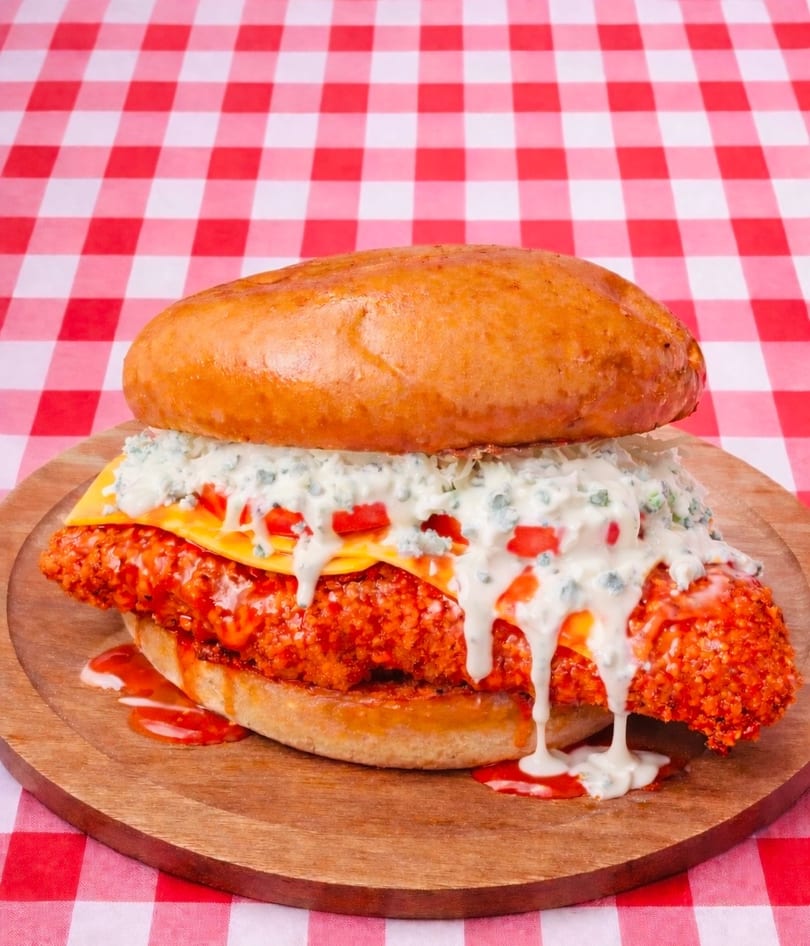 Spicy fried chicken sandwich with cheese, blue cheese dressing, and diced tomatoes on a bun.