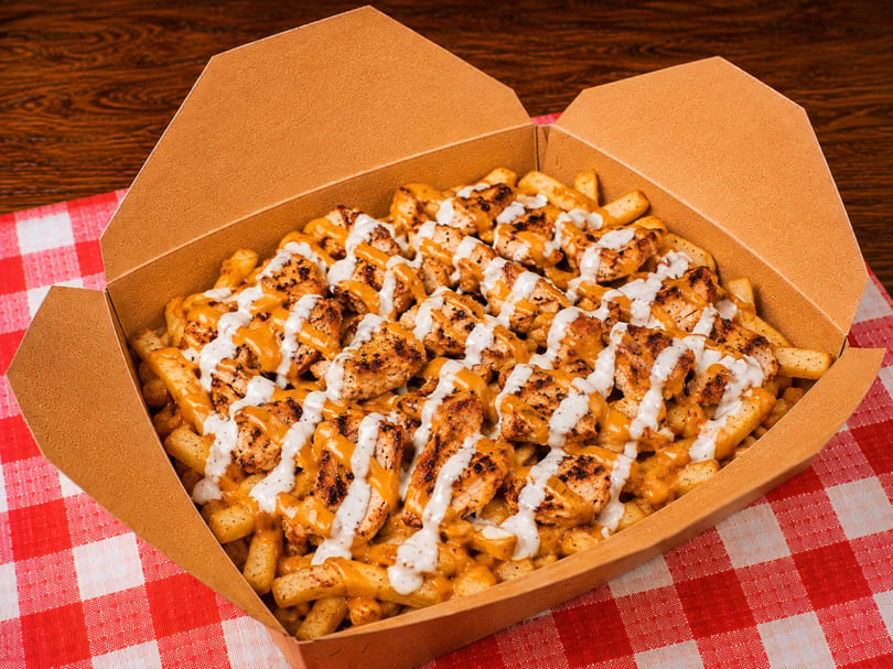 Loaded fries with grilled chicken, cheese sauce, and white garlic sauce in a takeout box.