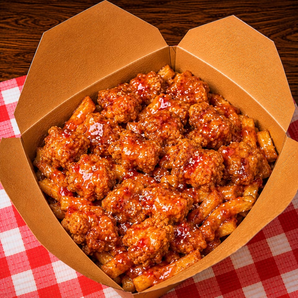 Crispy fried chicken bites and fries coated in a sweet and spicy sauce, served in a takeout box.