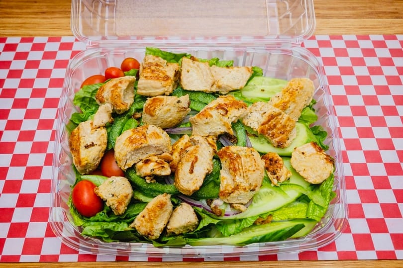 Grilled chicken salad with lettuce, tomatoes, cucumbers, and peppers in a plastic container.